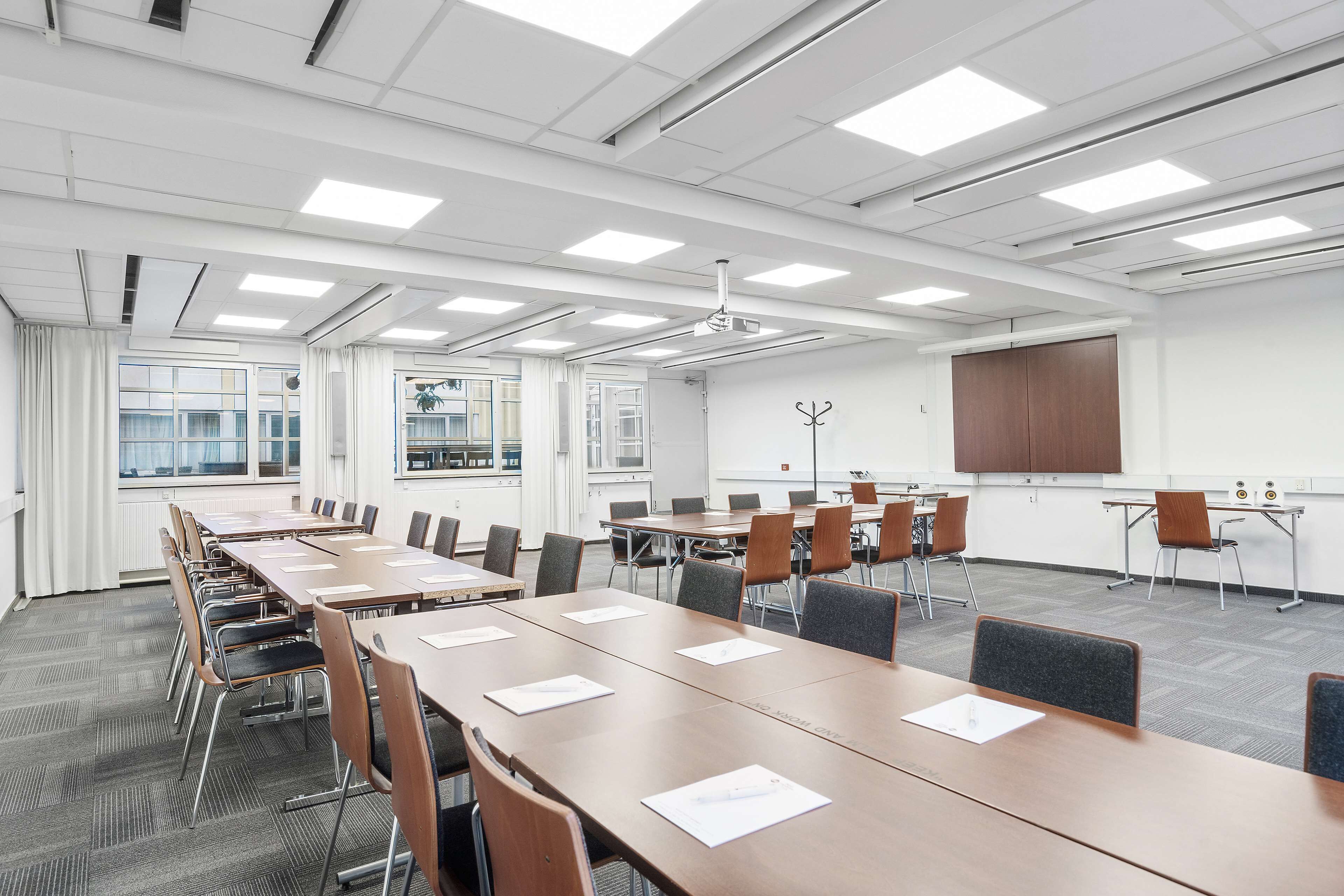 Une salle de conférence équipée de longues tables, de chaises, d’un écran de projection et d’un tableau blanc.