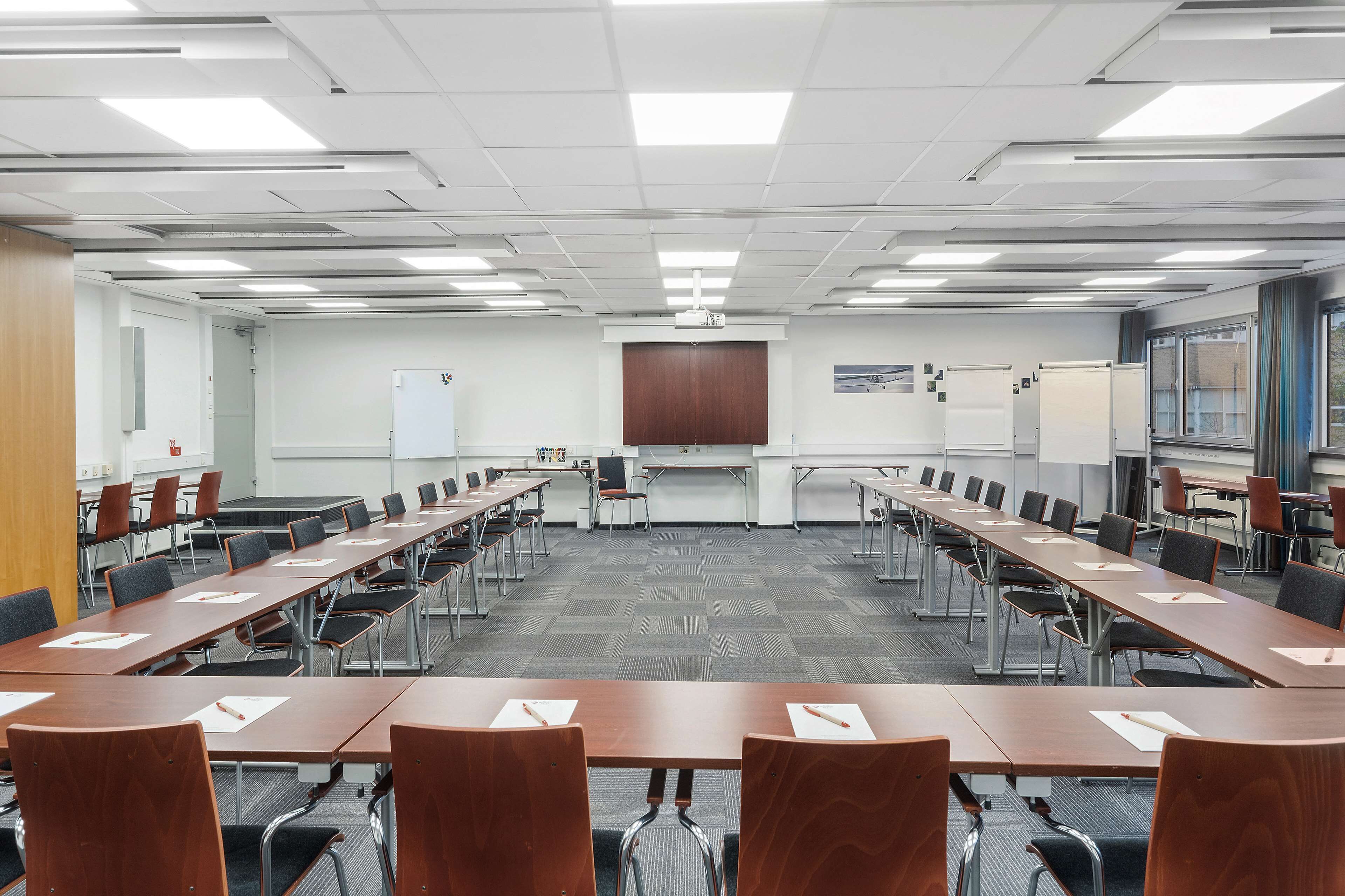 A conference room with long tables, chairs, a whiteboard, and a projector screen.