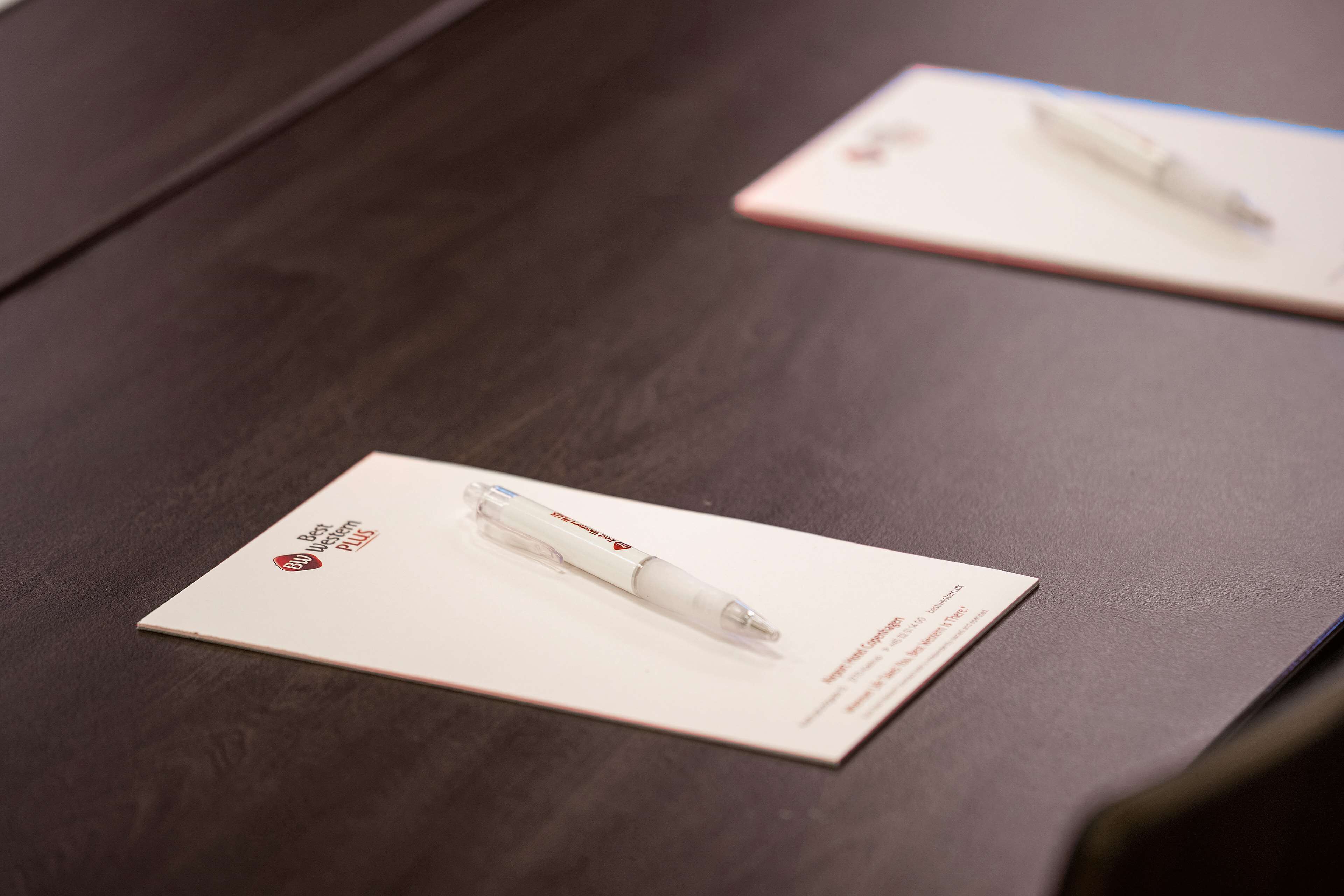 A dark wooden table with two white pens on white cards.