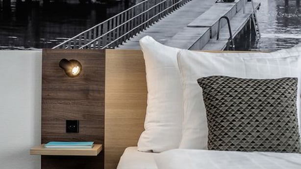 A modern hotel room with a wooden headboard, a bedside table with a lamp, and a view of a dock and water. - Best Western Plus Airport Hotel Copenhagen (Kastrup)