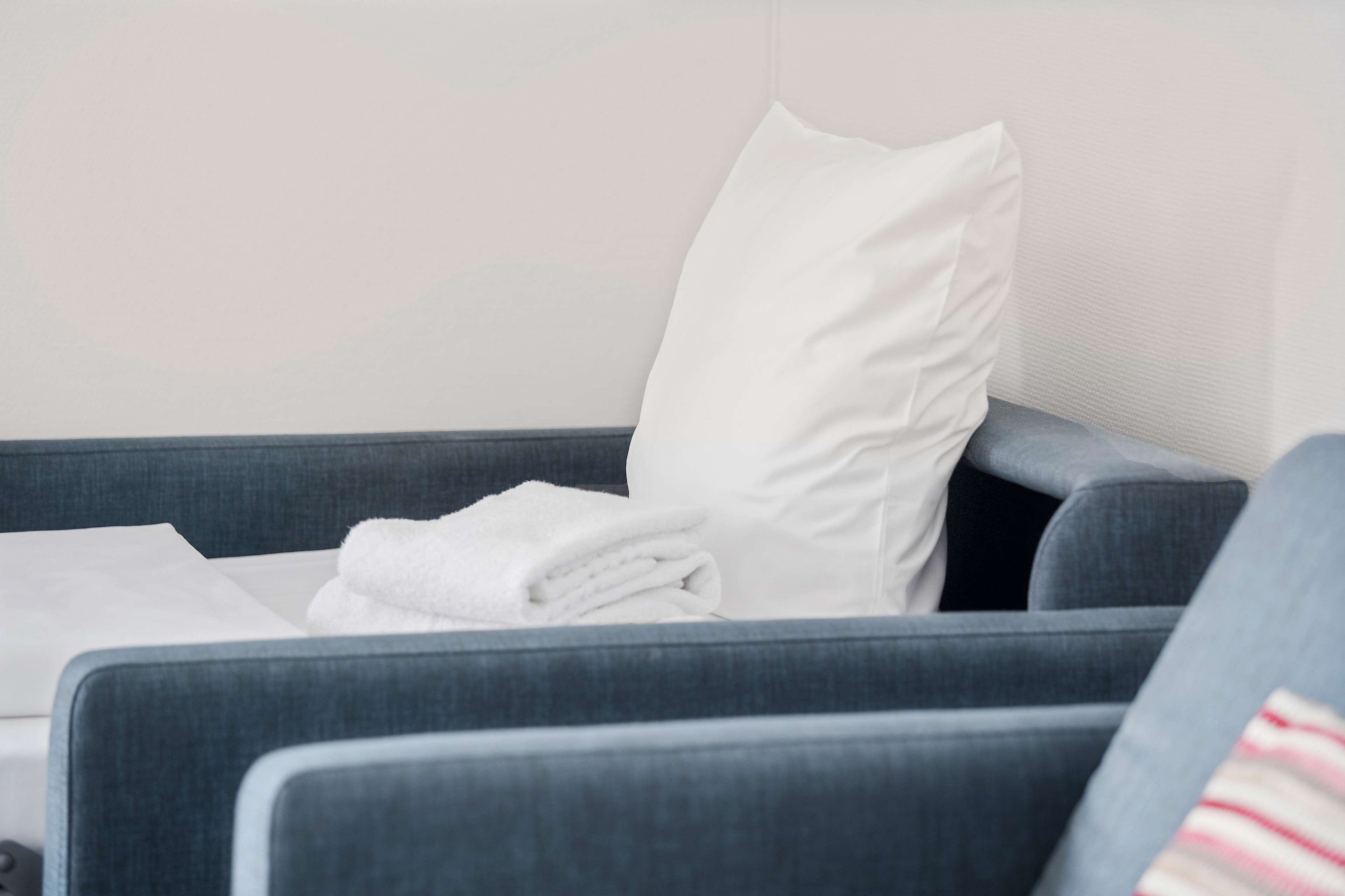 A hotel room with a grey sofa, a white pillow, and a neatly folded white towel.