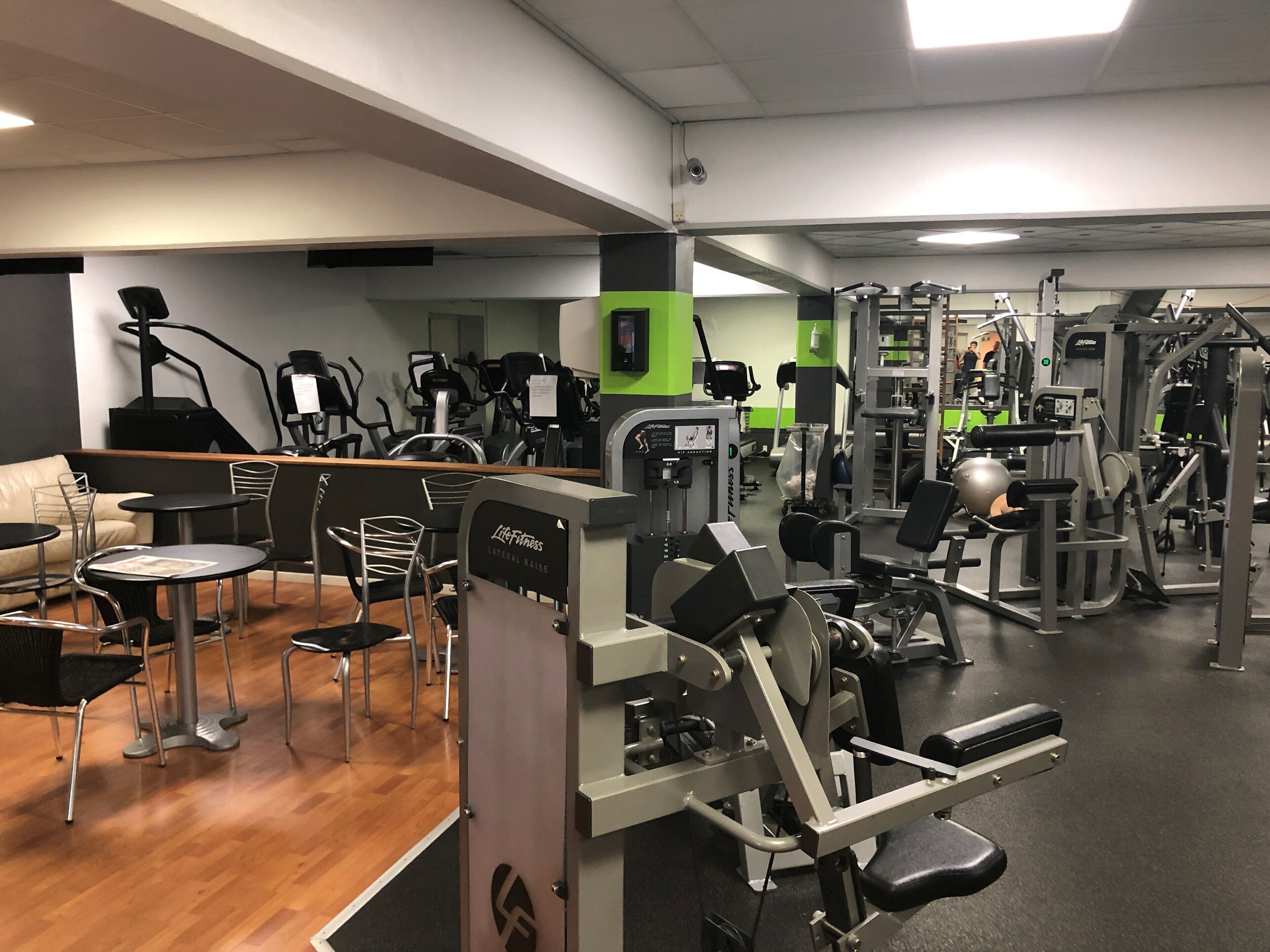 Een fitnessruimte met diverse trainingsapparaten, een loopband en een zithoek met stoelen en tafels.