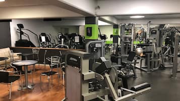 Een fitnessruimte met diverse trainingsapparaten, een loopband en een zithoek met stoelen en tafels.