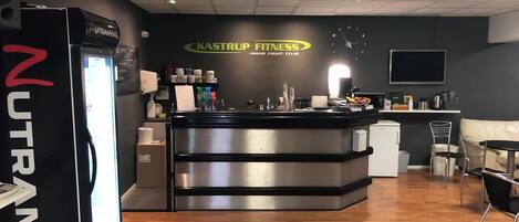 A fitness center with a reception desk, a refrigerator, and a wall-mounted clock.