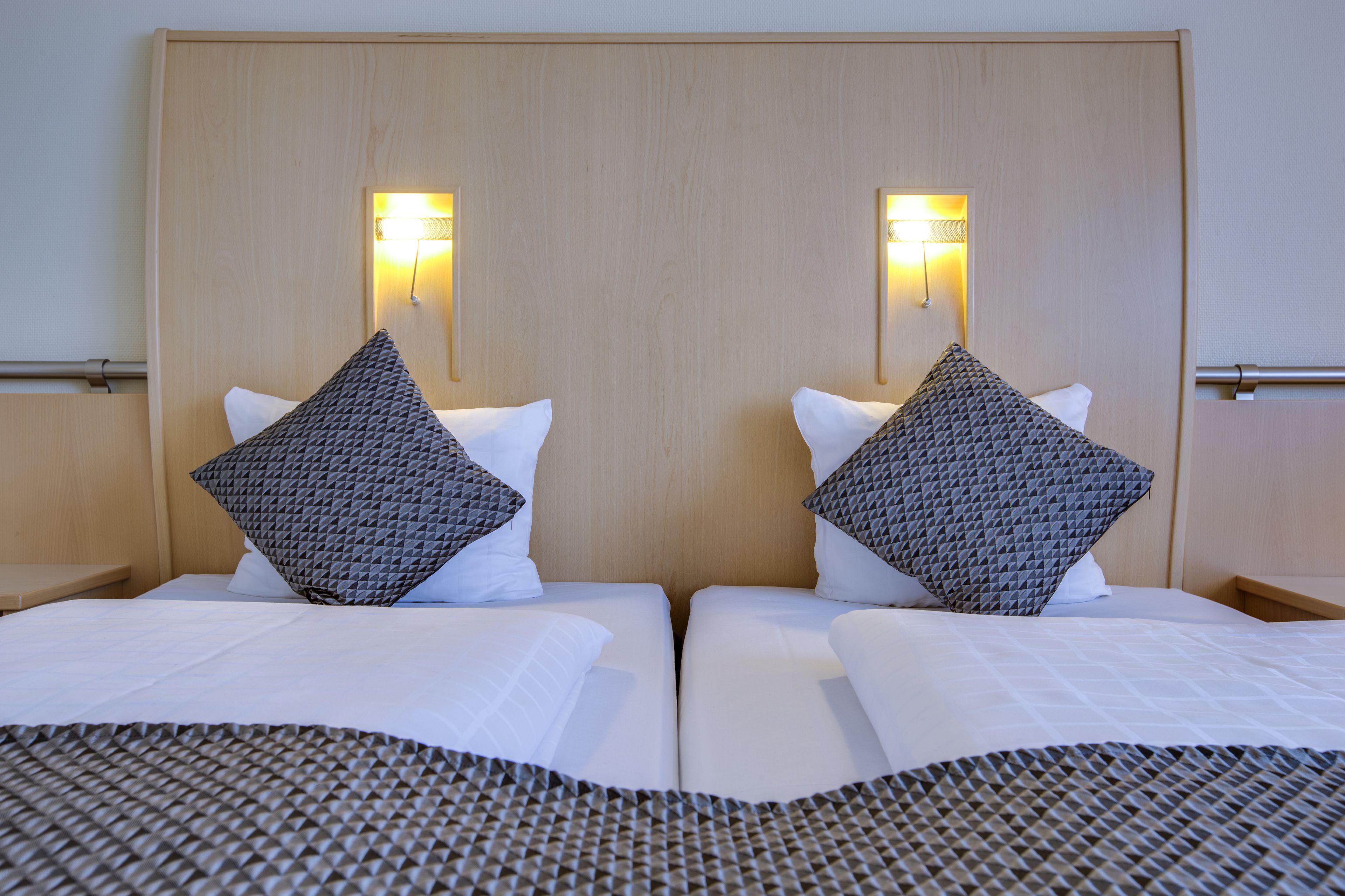 A hotel room with two beds, each with a headboard, white bedding, and patterned pillows.