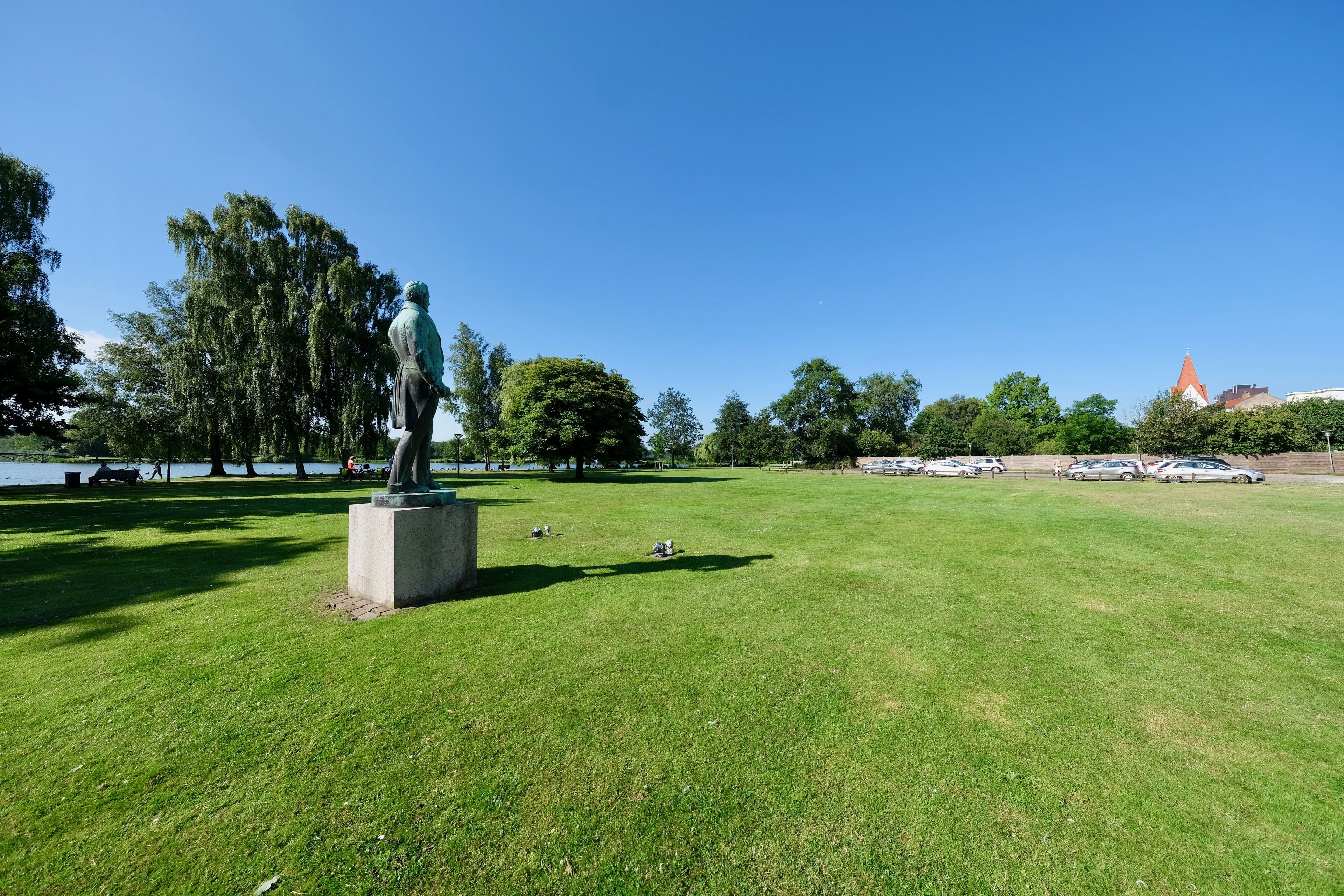 Un parque con una estatua, césped verde, árboles y un edificio a lo lejos.