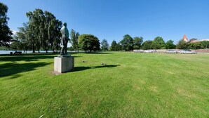 Un parque con una estatua, césped verde, árboles y un edificio a lo lejos.