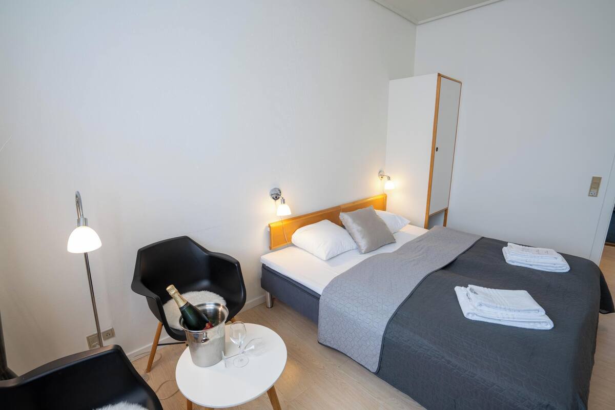 A hotel room with a bed, a chair, a small table, and a nightstand.