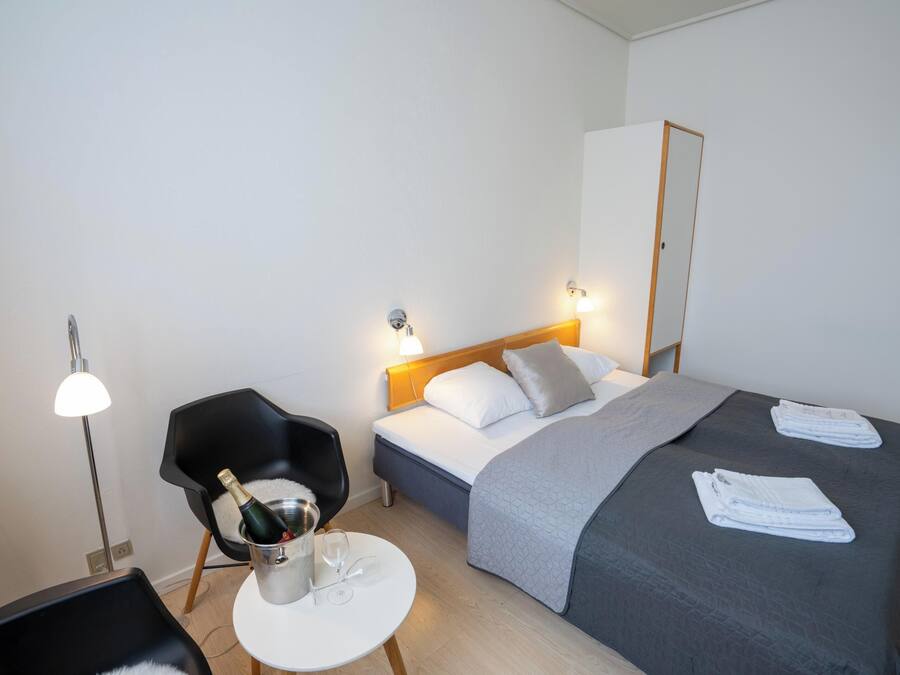 Una habitación de hotel con cama, una silla, una mesita y una mesita de noche.