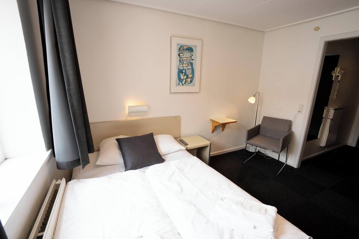 A hotel room with a bed, a chair, a desk, and a wall-mounted artwork.