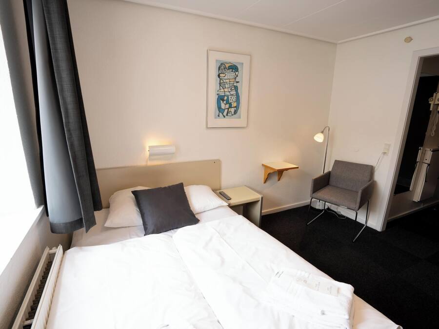 Habitación de hotel con cama, una silla, un escritorio y una obra de arte colgada en la pared.