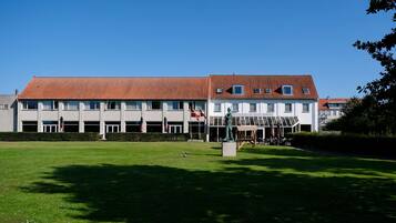 A building with a red-tiled roof, multiple windows, and a statue in the front lawn.