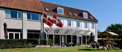 A two-story building with a tiled roof, large windows, and a glass entrance. Flags are displayed outside.