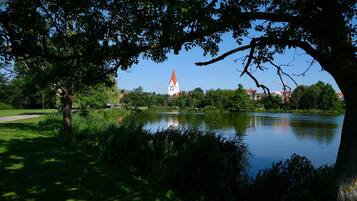 A serene park with a lake, lush greenery, and a distant church tower.