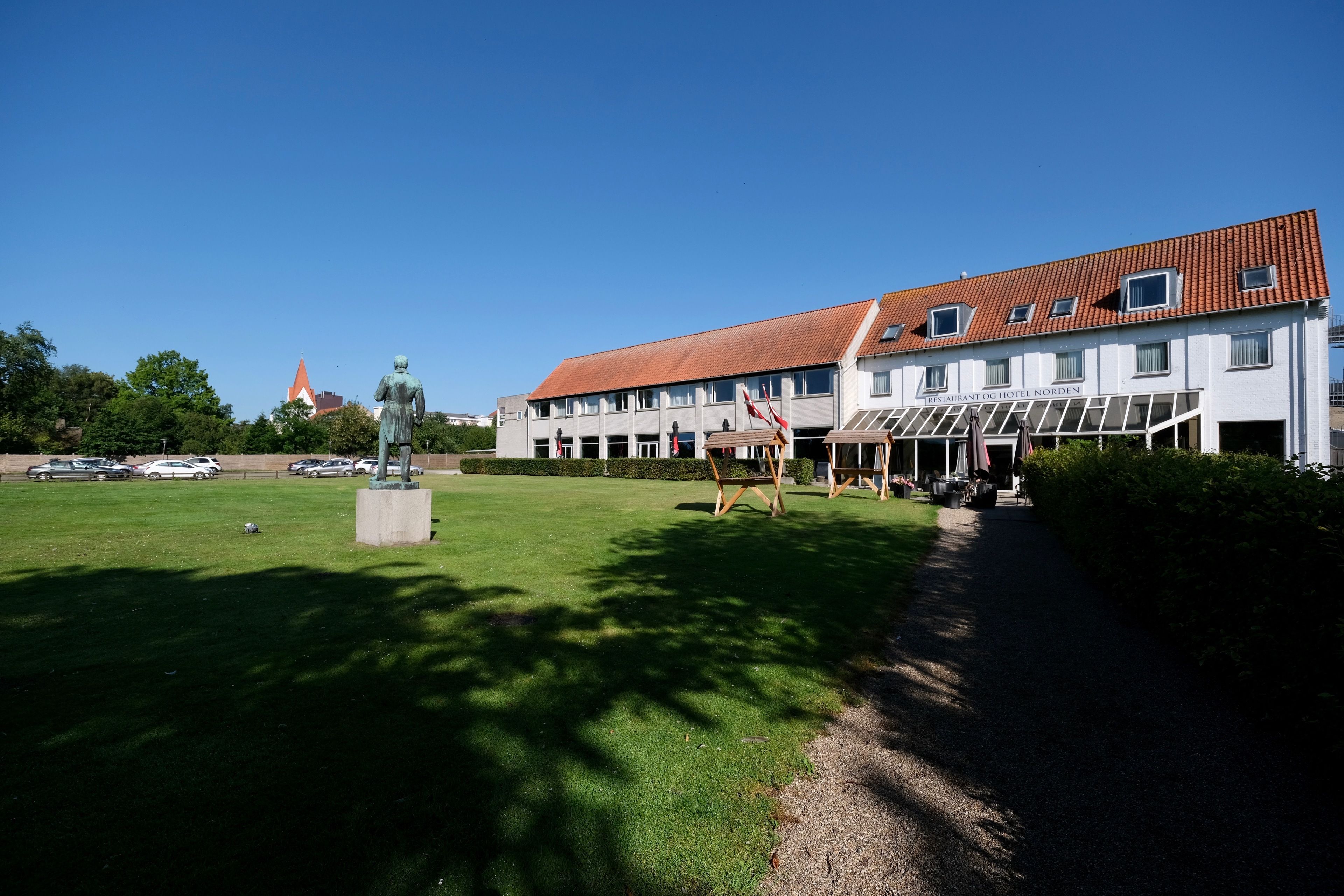 A hotel with a red-tiled roof, a statue in front, and a clear blue sky.
