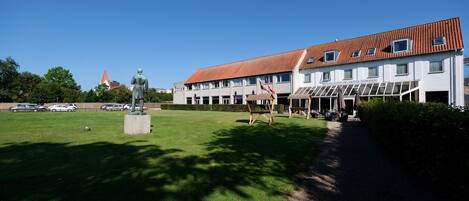 A hotel with a red-tiled roof, a statue in front, and a clear blue sky.