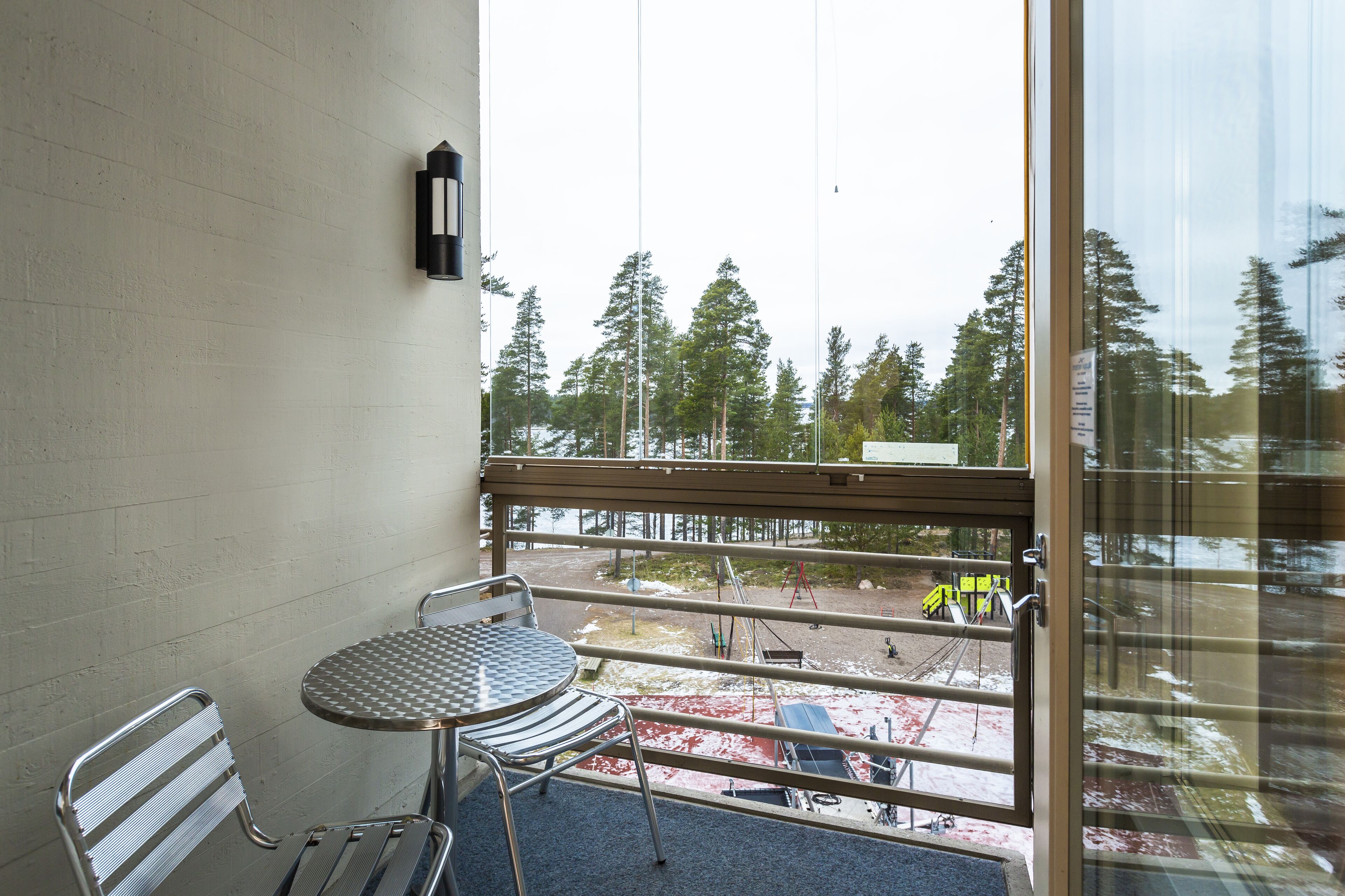 A balcony with a metal table and chairs, a metal bench, and a view of a construction site with trees.