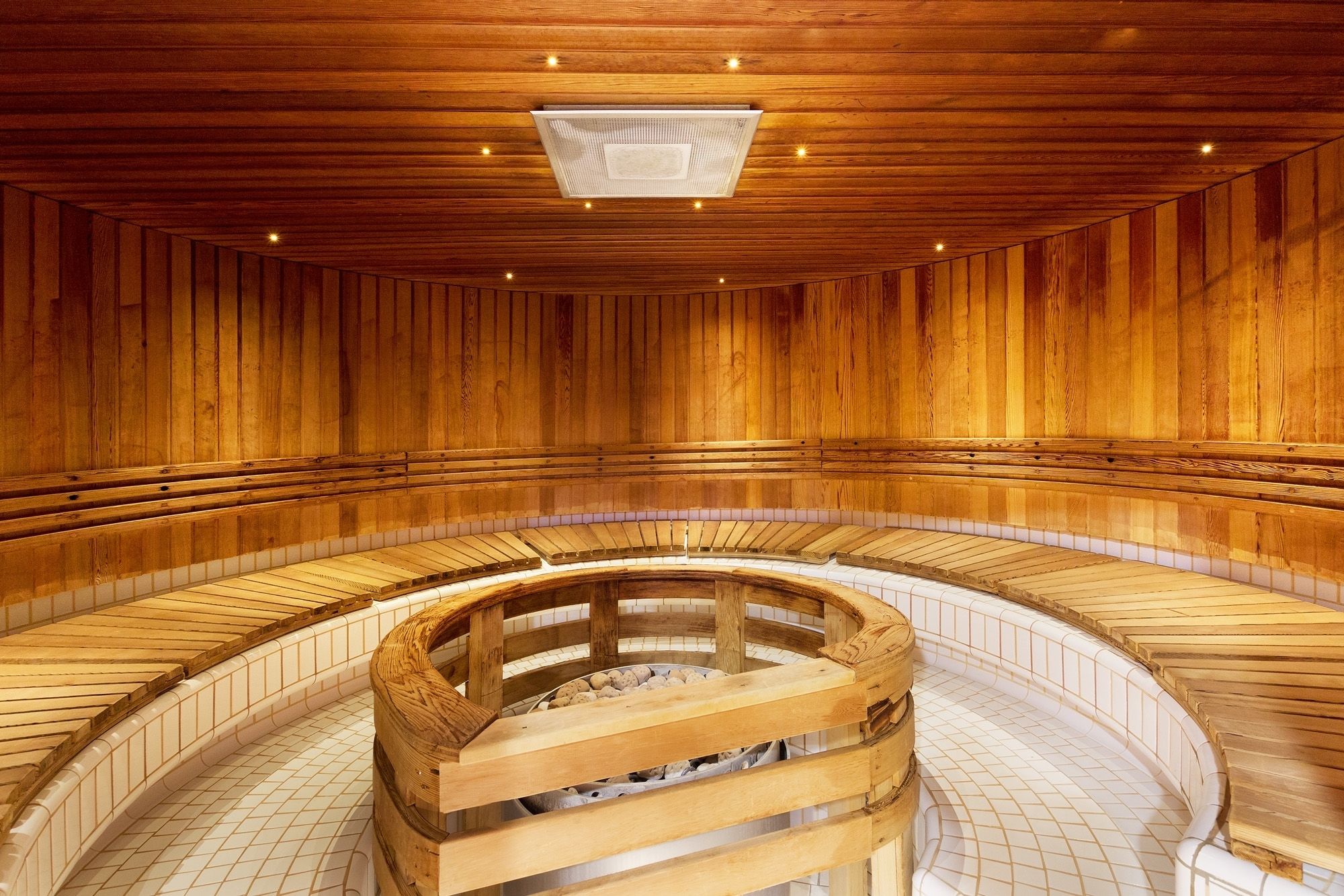 A wooden sauna with a central circular bench and tiered seating around it.