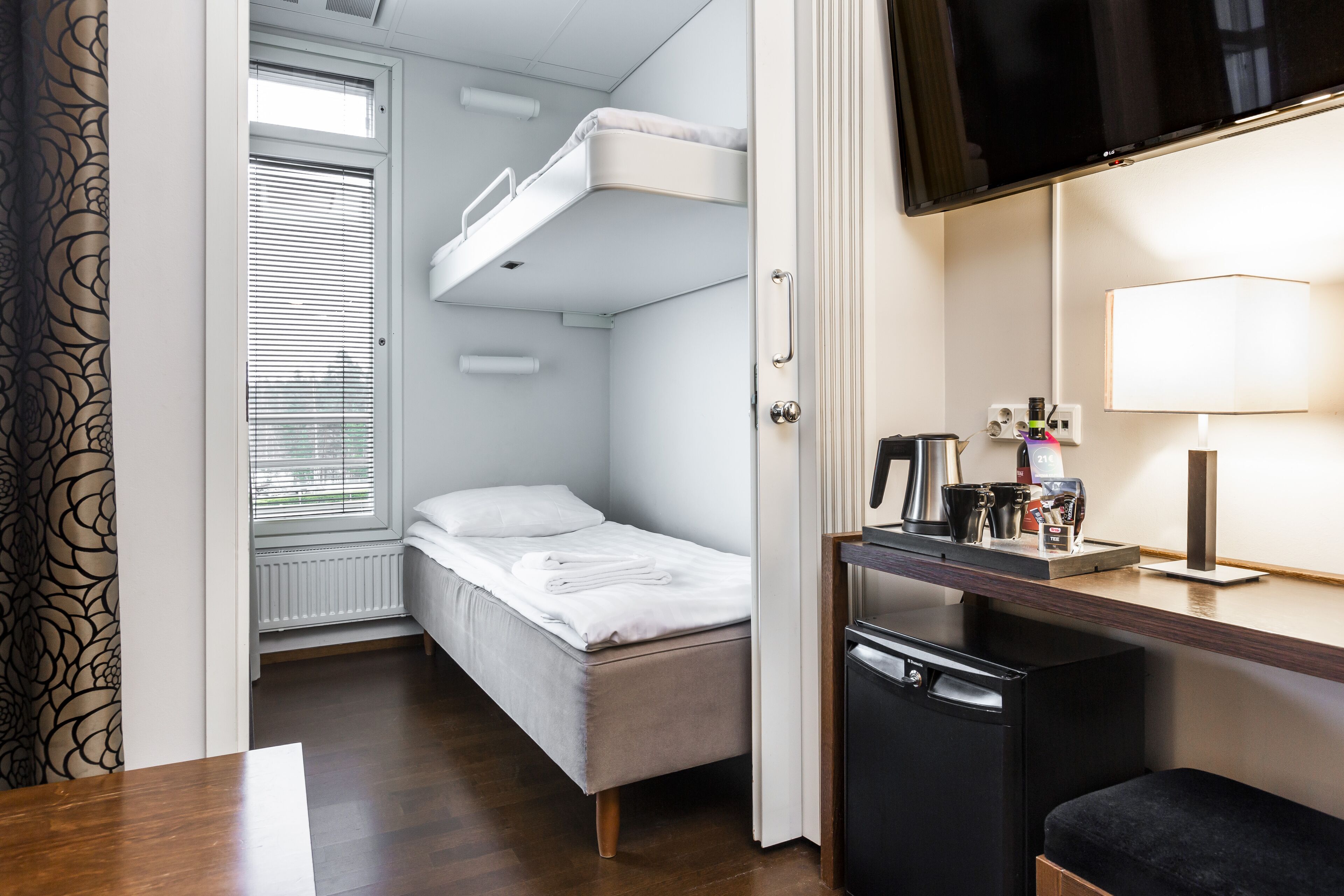 A compact room with a bunk bed, a small desk with a lamp, and a television mounted above the desk.