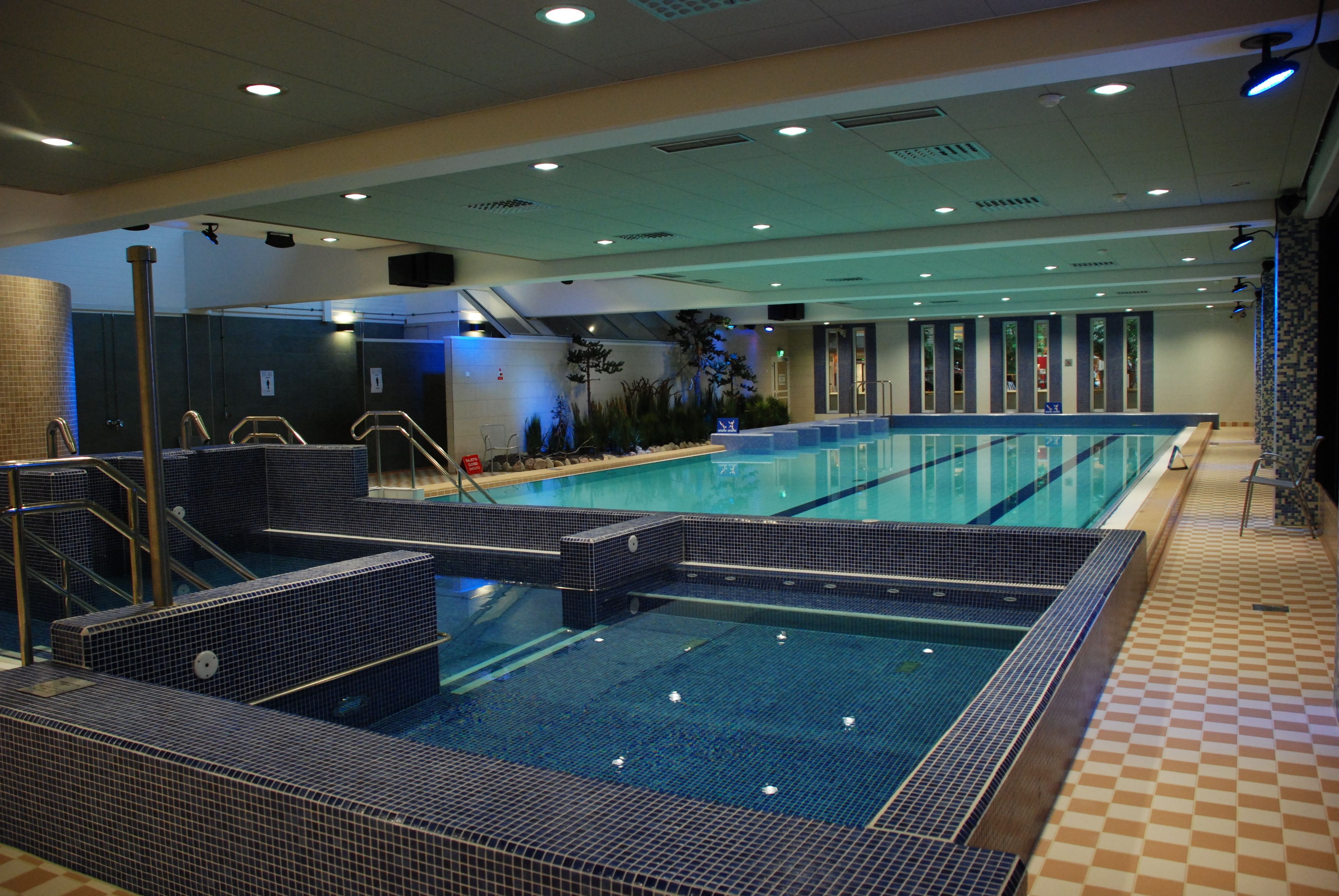 A large indoor swimming pool with multiple lanes, a changing room area, and a tiled floor.