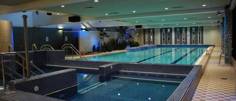 A large indoor swimming pool with multiple lanes, a changing room area, and a tiled floor.