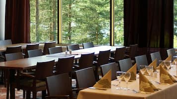 A conference room with multiple tables and chairs, large windows with a view of trees, and a carpeted floor.
