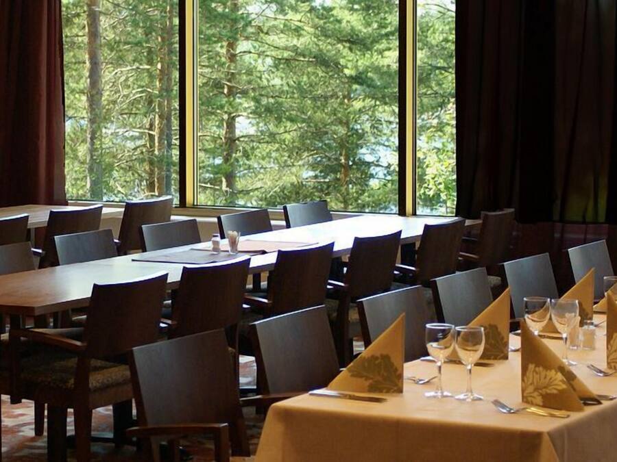 A conference room with multiple tables and chairs, large windows with a view of trees, and a carpeted floor.