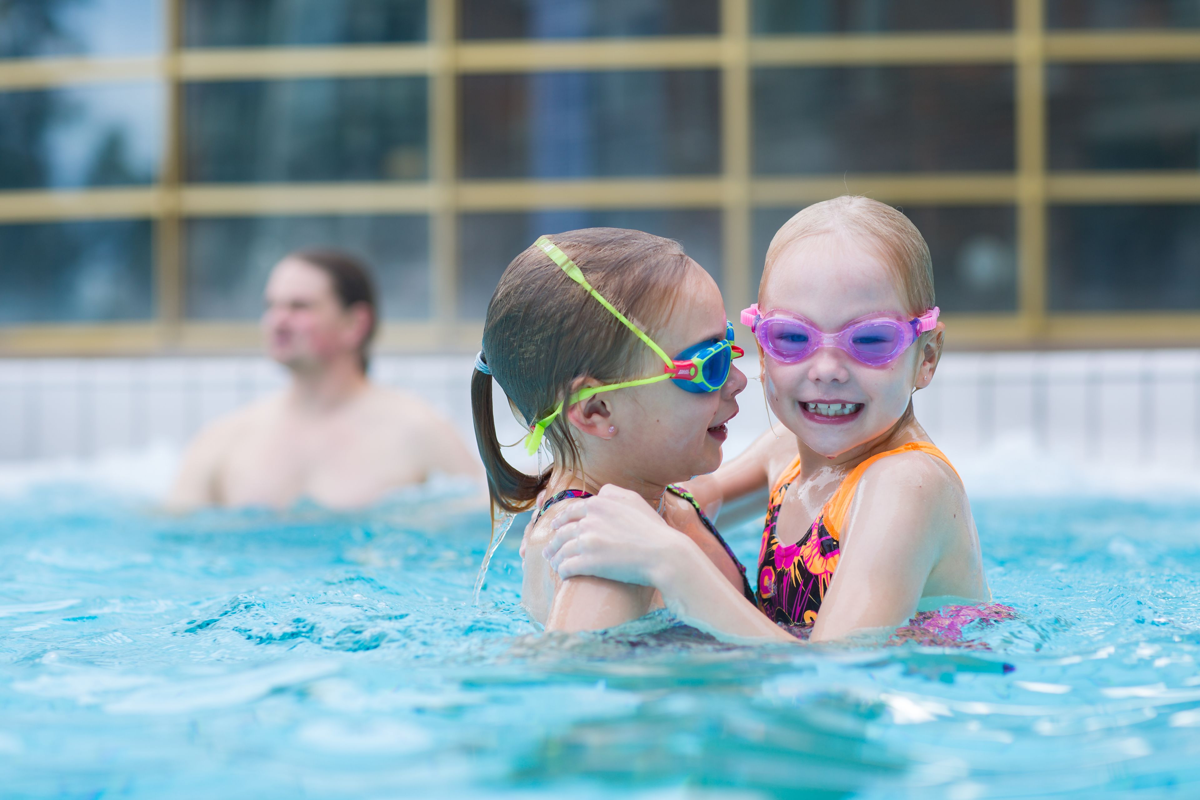 A swimming pool with two children in the foreground and a man in the background.