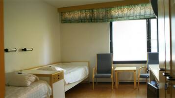 A small, simple room with two single beds, a desk, and a chair.