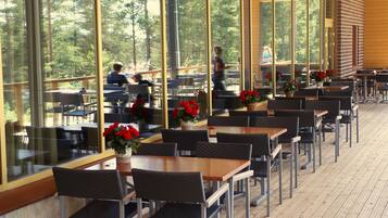 An outdoor dining area with tables and chairs, large windows, and potted plants.