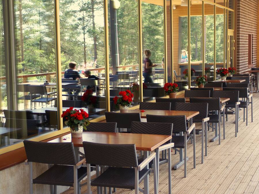 An outdoor dining area with tables and chairs, large windows, and potted plants.