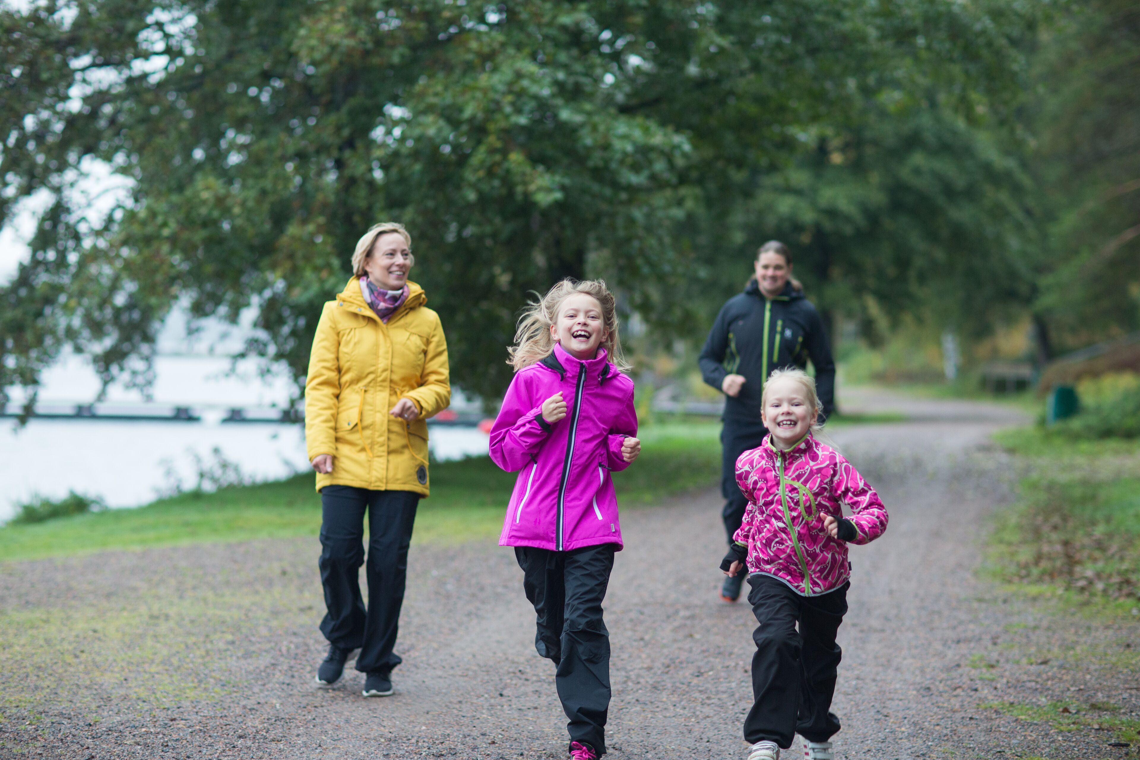 Three people jogging on a gravel path with a lake in the background.