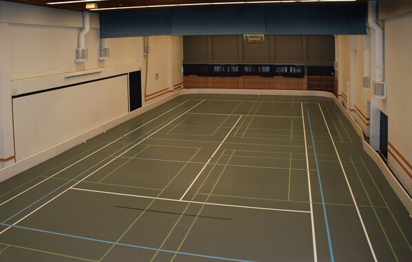 Un gimnasio interior con líneas delimitadoras para diferentes deportes, como baloncesto y tenis.