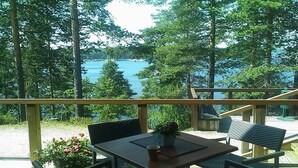 Una terraza con mesa y sillas que da a un lago, rodeada de árboles.