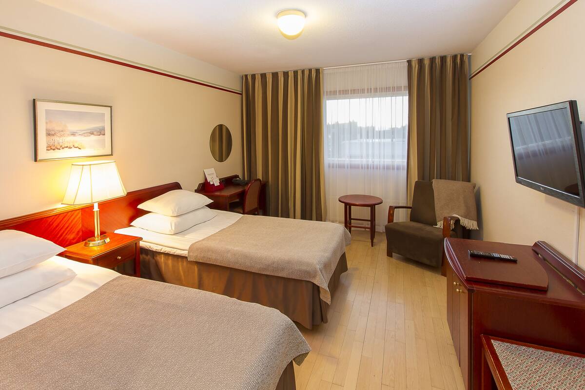 Een hotelkamer met twee bedden, een bureau, een stoel, een televisie en een raam met gordijnen.