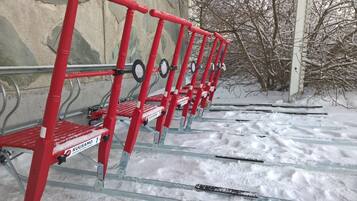 A row of red metal ski lifts with snow-covered ground and leafless trees in the background.