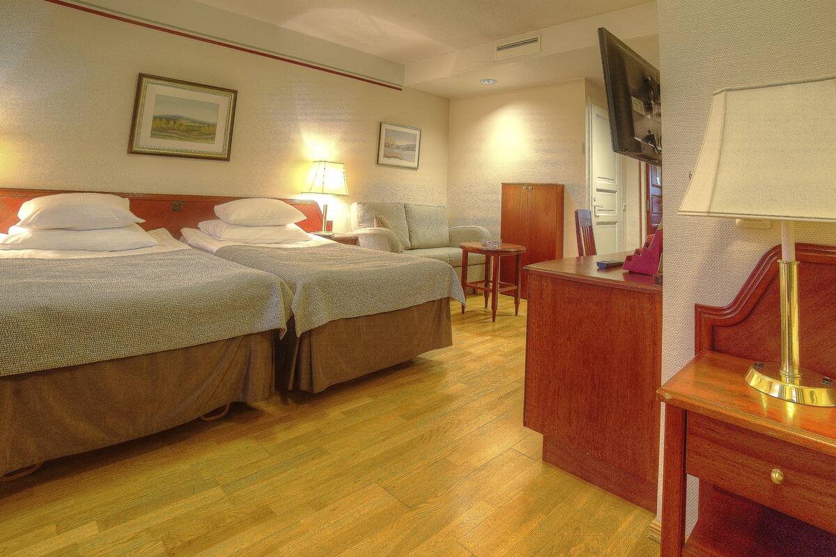 Een hotelkamer met twee bedden, een bureau, een stoel, een lamp en twee ingelijste foto's aan de muur.