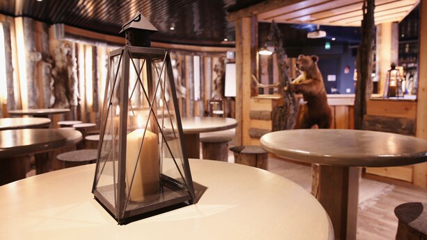 L’intérieur d’un restaurant avec des tables rondes, une bougie dans une lanterne, des murs en bois et des décorations à l’effigie d’ours.