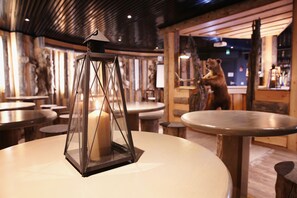 Een restaurantinterieur met ronde tafels, een kaars in een lantaarn, houten wanden en beren decoraties.