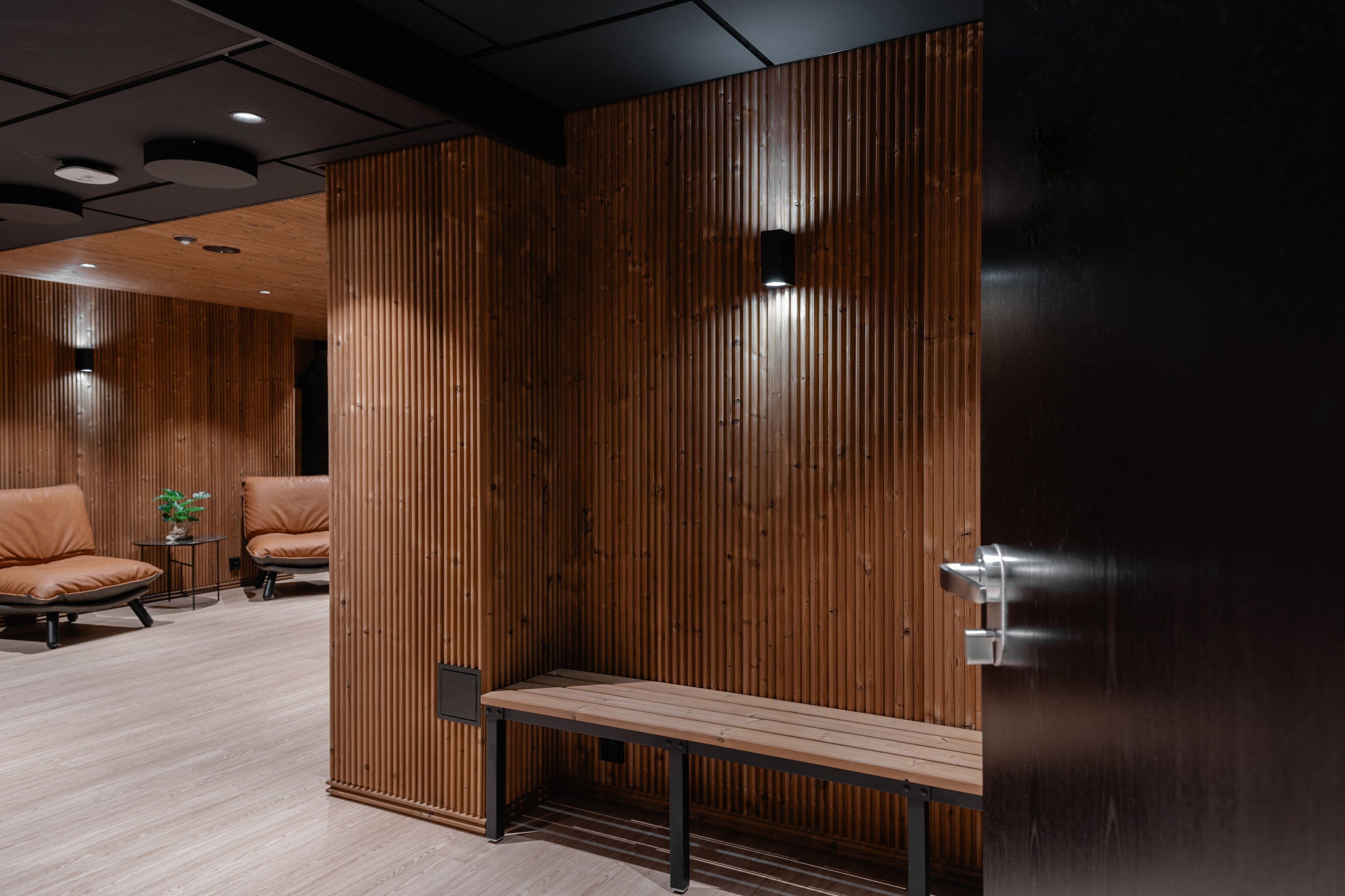 A modern interior with wooden panel walls, a bench, and leather chairs.