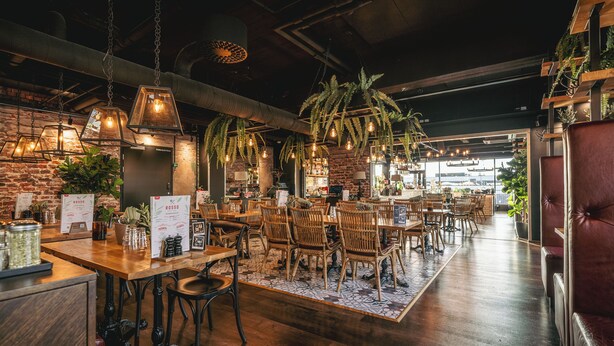 Un restaurant avec des tables et des chaises en bois, des suspensions décoratives et des murs en briques.