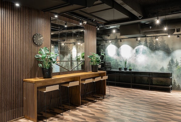 A modern interior with a wooden reception desk, potted plants, and a view of a forest through a misty window.