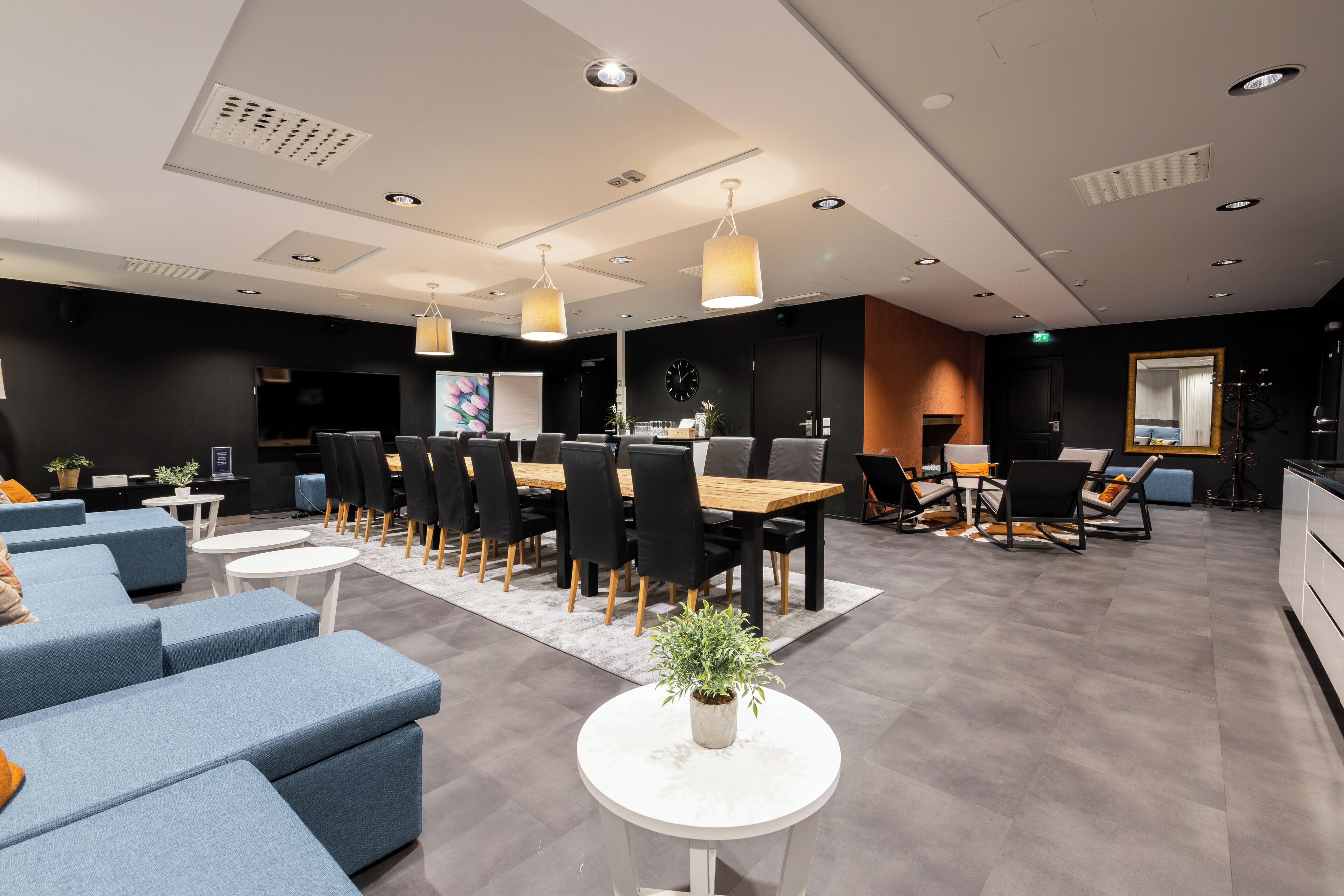 Un hall d’hôtel moderne avec un espace repas central, des canapés et une petite table agrémentée d’une plante.