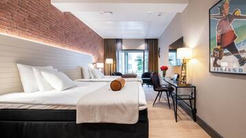 A hotel room with a brick wall, two beds, a desk with a chair, and a painting on the wall.