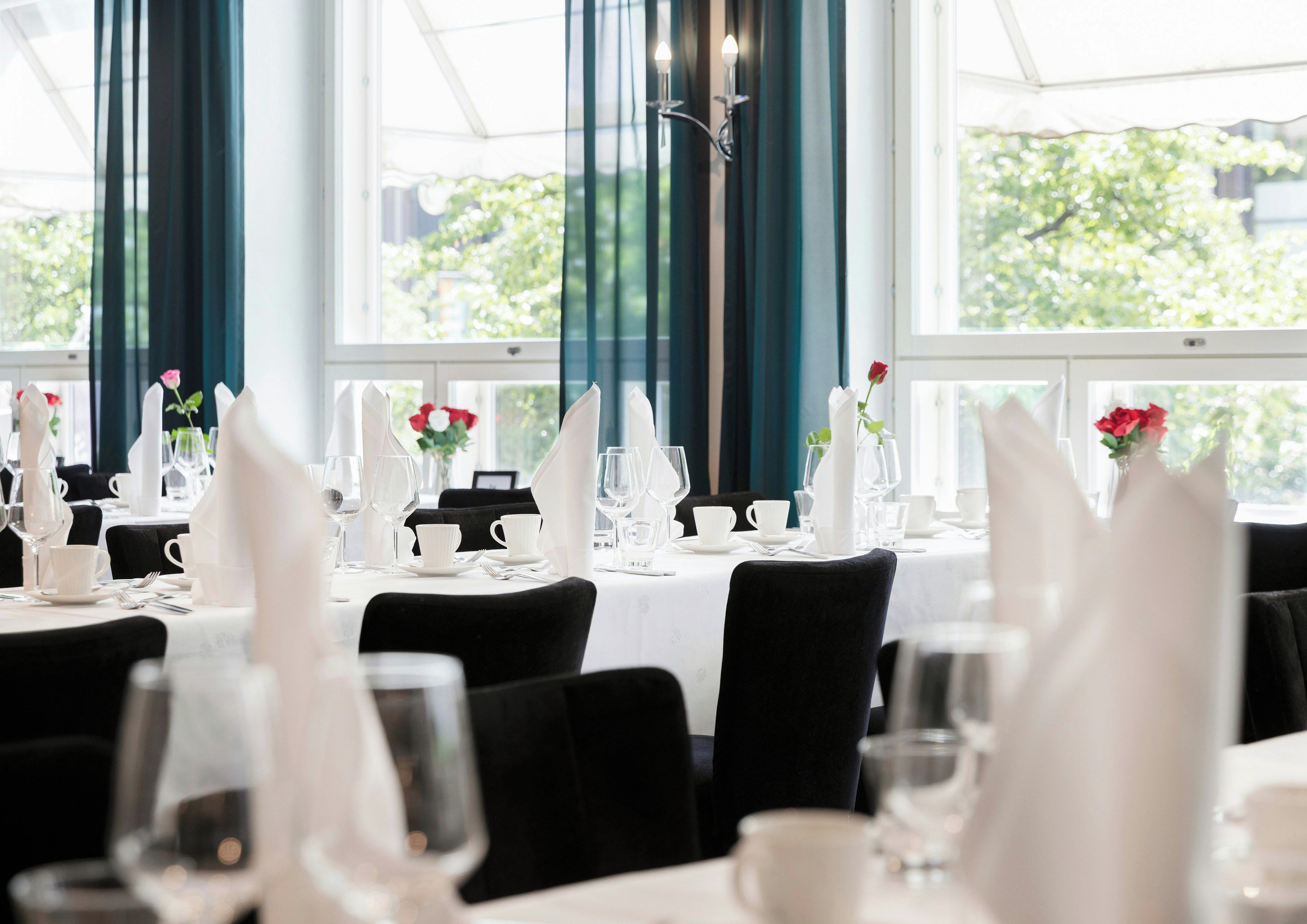 A restaurant with tables set for dining, featuring white tablecloths, black chairs, and floral centerpieces.