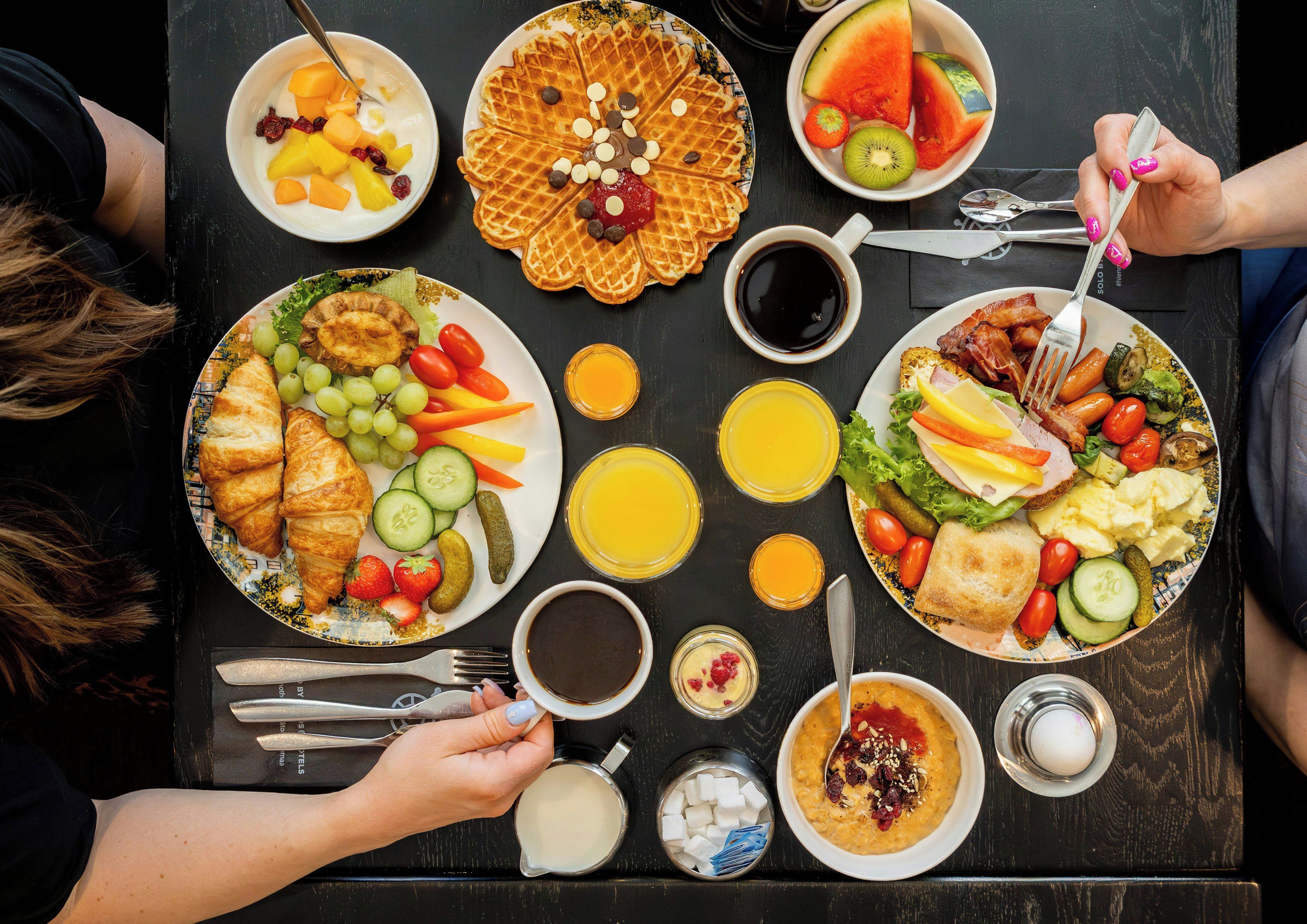 A table set with various breakfast items including waffles, fruits, vegetables, and beverages.