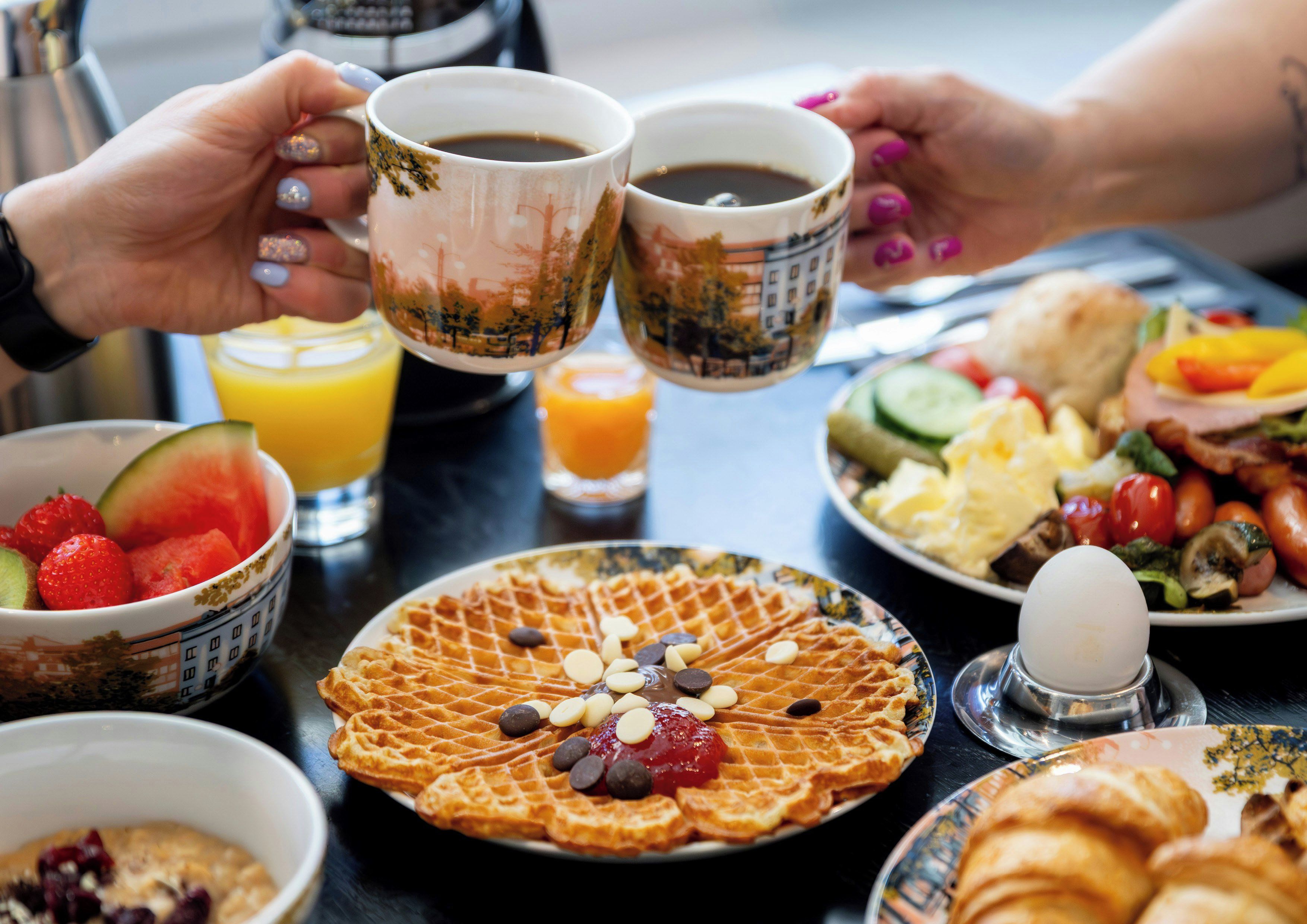 Une table dressée pour le petit-déjeuner avec des gaufres, des œufs et divers fruits.