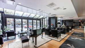 Un hall d’hôtel moderne, doté d’un grand piano, de sièges confortables et de grandes fenêtres offrant une vue sur la ville.