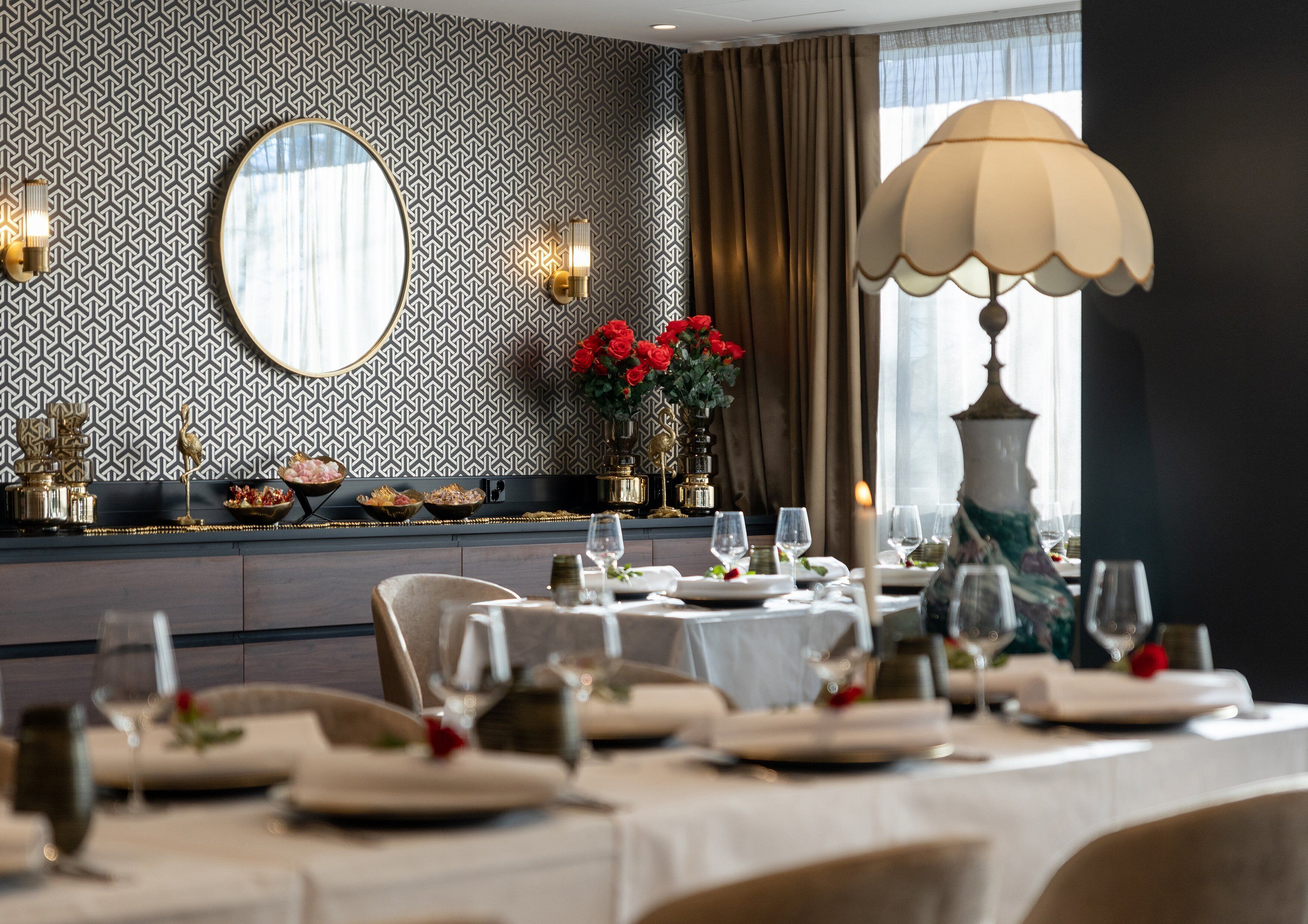 Un comedor con un papel tapiz estampado, un espejo grande y una mesa dispuesta para una comida.