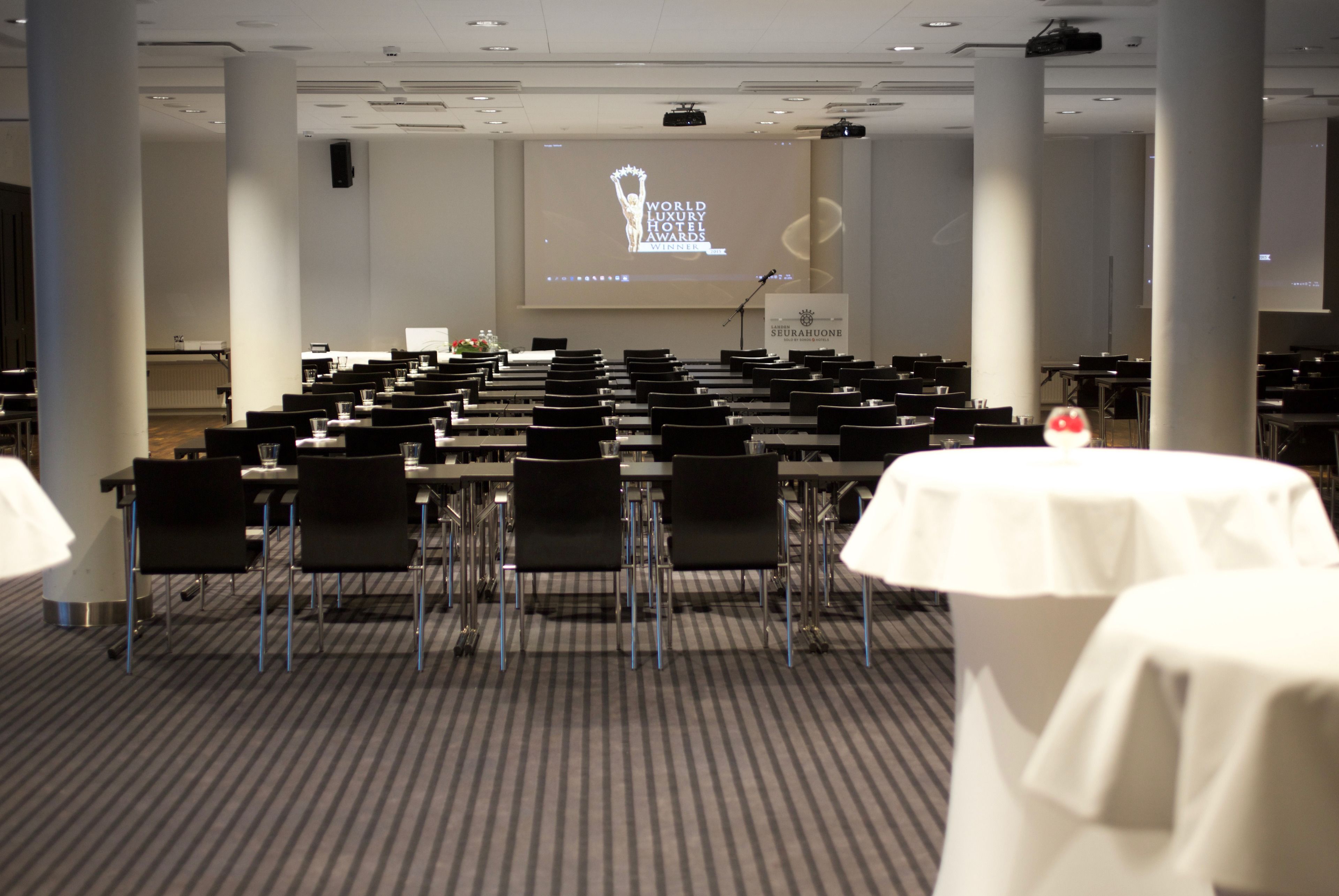 Ein Konferenzraum mit Tischen und Stühlen, einem Rednerpult und einem Bildschirm, der das Logo der World Luxury Hotel Awards zeigt.